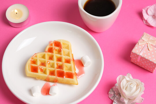 Close up view on home made heart-shaped waffle topped with strawberry syrup, a cup of coffee and a gift box. Romantic breakfast for valentine's day banner.