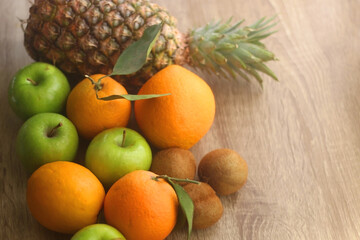 Pineapple, apples, oranges, lemons and kiwis on a wooden table. Selective focus.