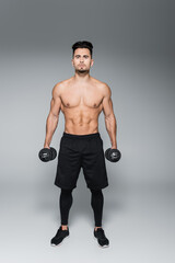 Fototapeta na wymiar full length of muscular sportsman working out with dumbbells on grey.