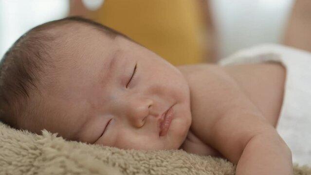4K close-up photo of face of an Asian newborn sleeping happily on a brown carpet.