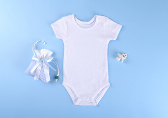 White cotton baby bodysuit mockup on blue pastel color background. Empty place for text or logo. Flat lay layout with baby boy clothes, ceramic nipple or baby's dummy, gift box