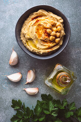 vista superior de un bol con hummus, dientes de ajo, aceite de oliva y perejil, sobre un fondo azulado
