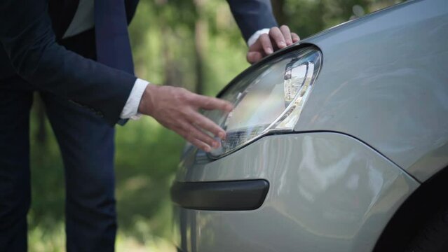 Male Caucasian hand touching headlight fixing car lights. Unrecognizable young male driver repairing broken vehicle part outdoors on summer spring day