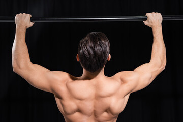 back view of muscular sportsman exercising on horizontal bar isolated on black.