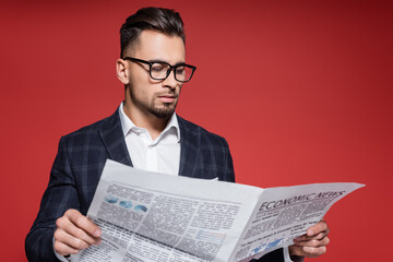 bearded businessman in blazer and glasses reading newspaper on red.