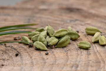 closeup the bunch green ripe cardamom with green leaves over out of focus wooden background.