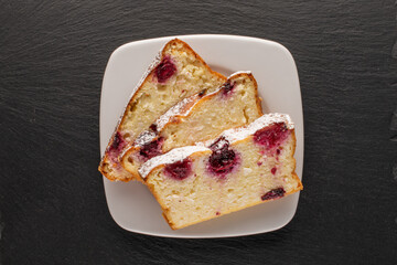 Three slices of homemade cottage cheese casserole with cherries on a white ceramic saucer on a slate stone, macro, top view.

