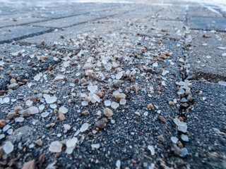 Salt grains on sidewalk surface in the winter. Applying salt to keep road clear and people safe in winter weather from ice or snow. Macro view of salt grains in sunlight in winter