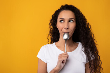 Excited Smiling Latin Lady Holding Spoon In Mouth - obrazy, fototapety, plakaty