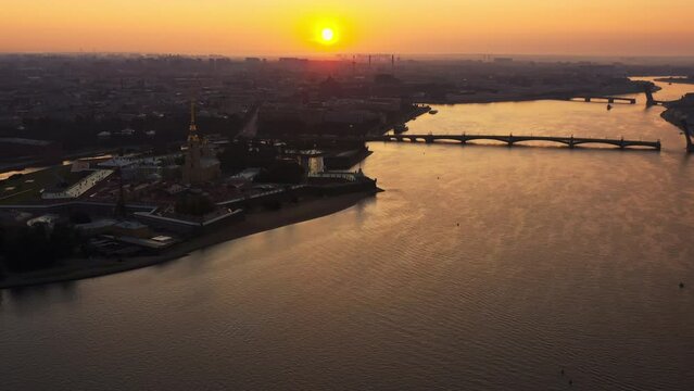 Drone flight over the Neva River to the Peter and Paul Fortress at sunrise, reflection of the orange sky on the water, drawbridges Troitsky and Liteiny are separated, 