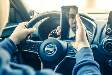 Teen drive a car and use smartphone. Young man reading messages holding a cell phone while driving....