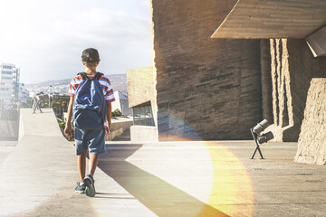 Back view of a young boy with backpack, strolling in a urban context. Trendy student walking out of the college after a day of school. Youth, new generation, leisure, teen and free time concept