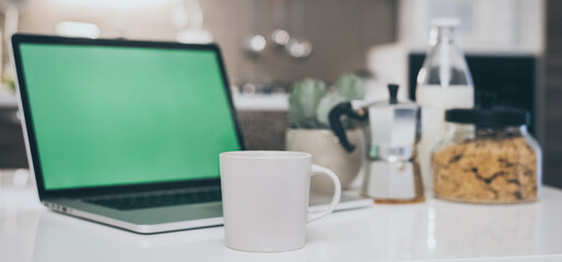 Table set for breakfast, kitchen in the background. Natural meal and technology devices. Interior view of a cozy and modern home. Millennial, youth, home working, home schooling, remote work concept.