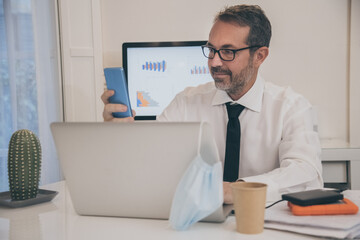 Business man with surgical masks working in the office during lockdown for coronavirus covid-19. Male sitting at the desk works with laptop at home. Health care, quarantine, remote working concept.