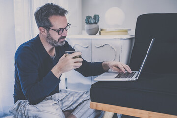 Man works with laptop sitting on the ground at home. Male working at home with remote office. Boy use online devices in the living room. Homeworking, home schooling lifestyle new communication concept