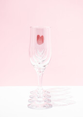 Creative  Valentines Day love minimal composition made of a linear series of champagne glasses one after the other with a red heart in the farthest glass on two color pastel pink and white background.