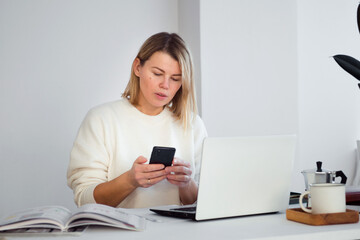 female freelancer online working at table using smartphone, young woman using laptop for business communication or video chatting