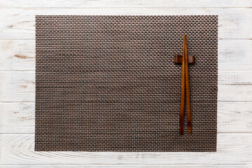 Two chopsticks and bamboo mat on wooden background. Top view, copy space