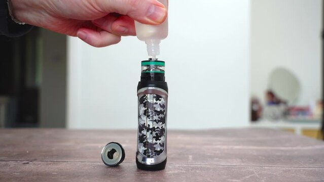 pouring e liquid vape juice into the open top of an electronic cigarette e-cig sub ohm atomiser and glass tank