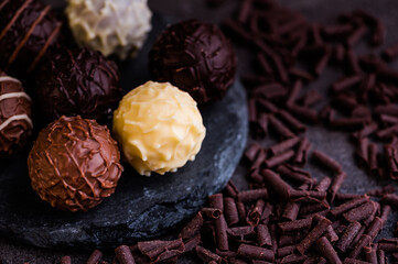 chocolate truffles on a small slate against dark background beside are lying chocolate flakes