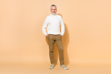 Fototapeta na wymiar Full length body size view of attractive cheerful grey-haired man holding hands in pockets isolated over beige pastel color background