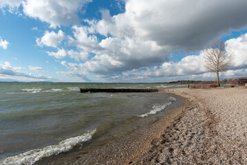 Ufer am Chiemsee mit Strand bei Sturm, Wolken, brechenden wellen, Bäumen, Steinen  und Sonneschein