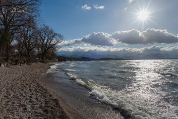 Ufer am Chiemsee mit Strand bei Sturm, Wolken, brechenden wellen, Bäumen, Steinen  und Sonneschein