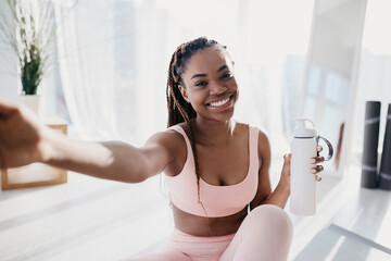Smiling young African American lady with bottle of water taking selfie on break from home workout