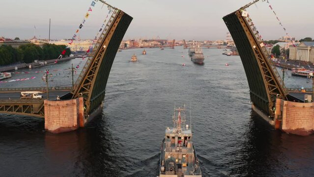 Aerial landscape with warships in the Neva River before the holiday of the Russian Navy at early morning, warships pass under a raised drawbridge, the latest cruisers among landmarks, Palace bridge