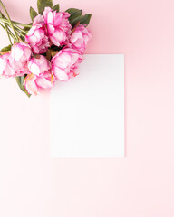 Minimal aesthetic flower bouquet scene with blank white paper on light pink pastel background. Flat lay. Copy space.