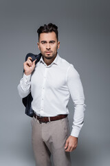 Naklejka premium young bearded businessman in white shirt holding blazer isolated on grey.