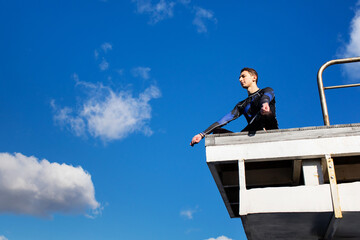 A young swimmer in a swimming suit is sitting in the pool on a diving tower in the lotus position and resting