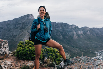 Fit woman in sports clothes holding backpack on a top of a mountain. Female hiker relaxing and...