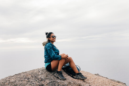 Smiling woman sitting on the cliff looking at the view. Female hiker resting on a rock looking away.