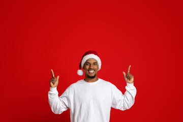 Charismatic african american guy in Santa hat pointing up