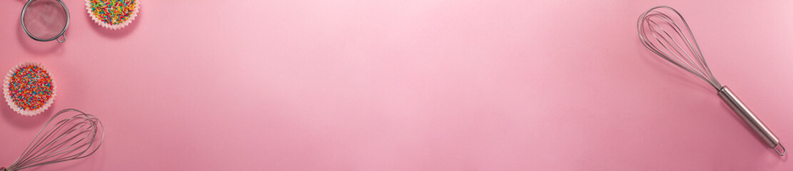 Banner of cupcake liners with colored sugar inside whisk and strainer flat lay top view. Confectionery cooking concept with copy space on bright pink paper. National cooking day