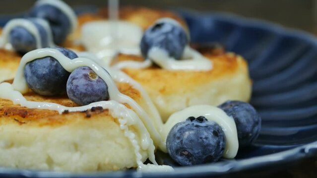 white condensed milk flows on cottage cheese pancakes with blueberries on a ceramic blue bowl. Delicious healthy natural breakfast for the whole family