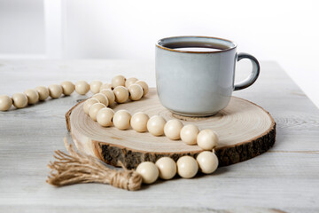 A blue ceramic cup on a wooden round cut, beads, a rosary for prayer on a beige table against a white wall. Place for text