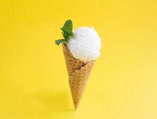 Close-up on vanilla ice cream in a waffle cone on the yellow background. Copy space.
