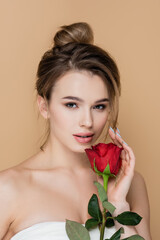 charming woman with naked shoulders looking at camera near red rose isolated on beige.