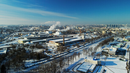 Industrial area on the outskirts of the city. Factory buildings are covered with snow. Factory pipes are visible. Winter industrial landscape. Aerial photography.
