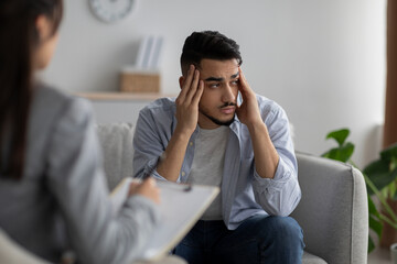 Depression counseling. Desperate arab man telling about unhappy life while female psychologist taking notes