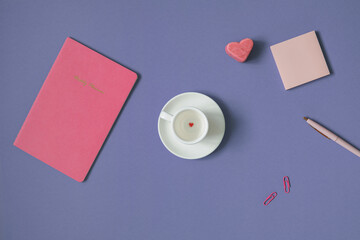 Flat lay of weekly planner, blank paper sheets, stationery, white cup with small red heart-shaped candy on the bottom. Top view, trendy pink and very peri colors. 