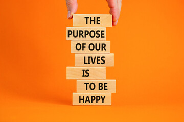 Purpose of happy lives symbol. Wooden blocks with words The purpose of our lives is to be happy. Beautiful orange background, copy space. Businessman hand. Business, purpose of lives is happy concept.