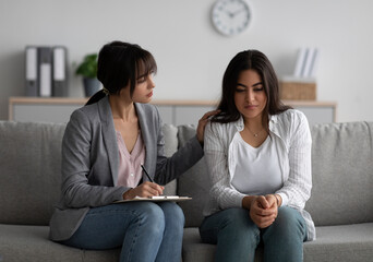Professional psychologist supporting unhappy middle eastern woman during psychotherapy session, assisting female patient