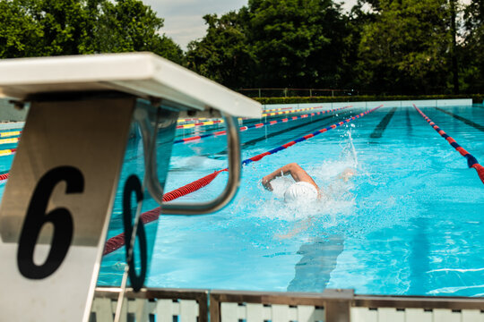 A Caucasian male swimmer doing the front crawl stroke, swimming in the freestyle. View from a poolside, behind a starting block.
