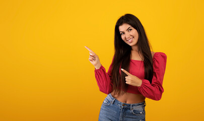 Happy young armenian lady pointing two fingers aside at free space advertising your text or design,...