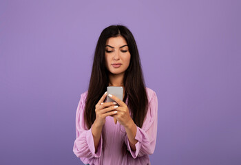 Gadget addiction concept. Serious armenian lady texting on smartphone or surfing internet, violet background