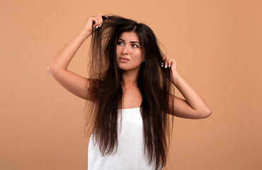 Frustrated armenian woman showing her damaged long locks, having bad hair day, upset over her messy...