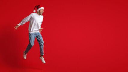 Fototapeta na wymiar Amazing Offer. Shocked Man Wearing Santa Hat Jumping On Red Background